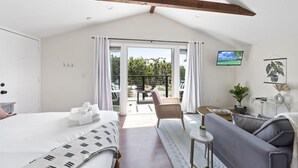 Une chambre avec un lit, un canapé, une petite table, une télévision et un balcon avec vue.