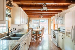 A kitchen with wooden beams, a granite countertop, a dining table with chairs, and a stove.
