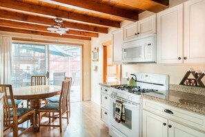 A kitchen with white cabinets, a stove, a microwave, and a dining area with a table and chairs.