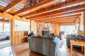 A cozy cabin interior with a stone fireplace, wooden ceiling beams, and a comfortable seating area.