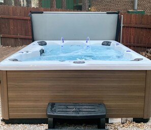 A hot tub with a wooden exterior, a control panel, and a small step leading into it.