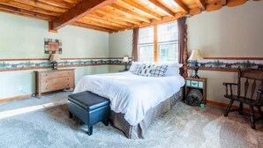 Una camera da letto con soffitto in legno, un letto con biancheria da letto bianca, un comodino, una lampada e una finestra con vista.