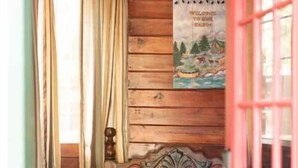Interno di una casetta in legno con una panca, un poster appeso al muro e una porta rossa.