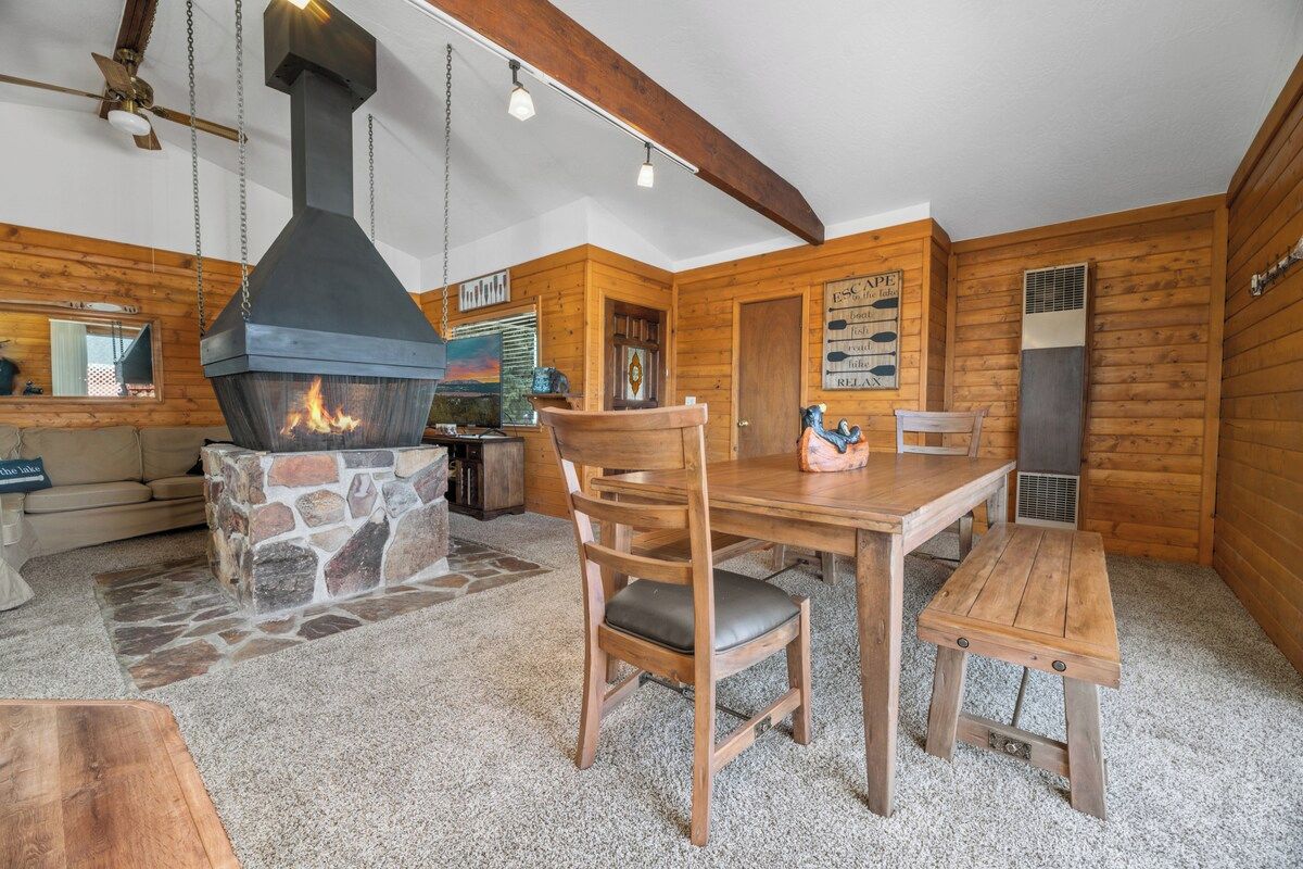 Een gezellig blokhutinterieur met een stenen open haard, houten wanden, een eettafel en een bank.