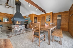 Een gezellig blokhutinterieur met een stenen open haard, houten wanden, een eettafel en een bank.