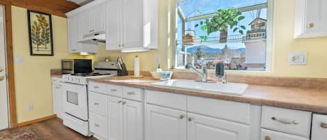 A kitchen with white cabinets, a stove, a sink, and a window with a view of greenery.