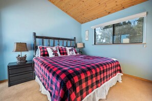 A bedroom with a bed, nightstands, a window, and a ceiling with wooden beams.