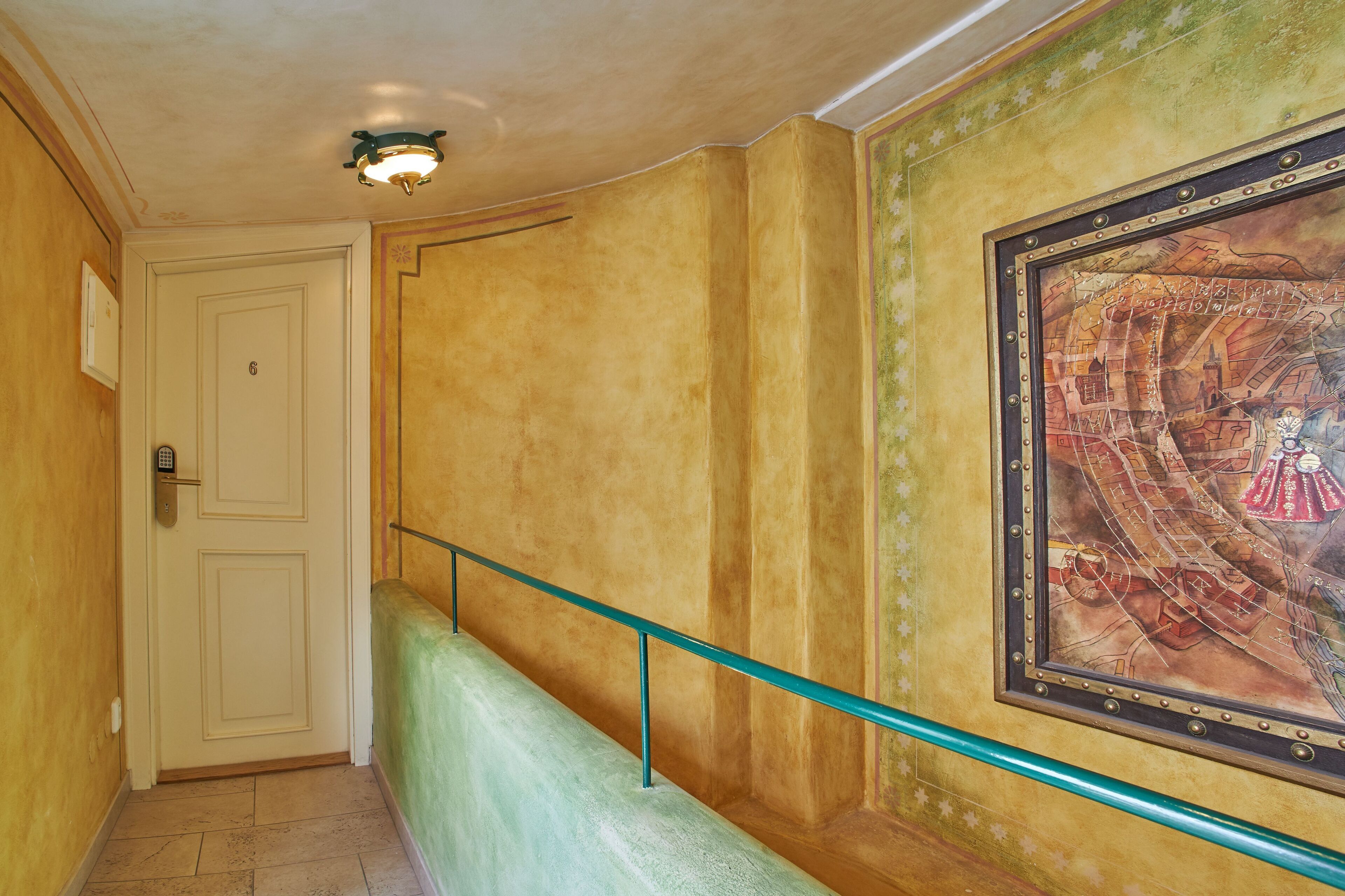 A hallway with a door marked with the number 6, a green cushioned bench, and a framed mural on the wall.