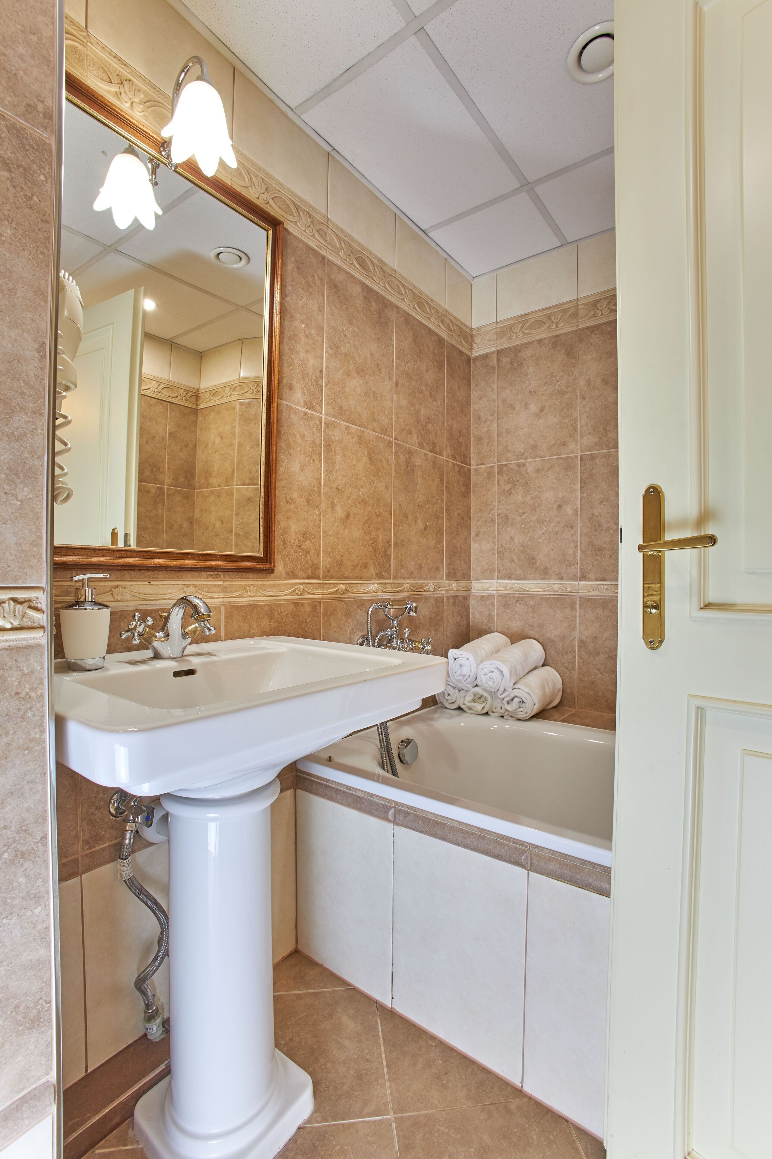A bathroom with a pedestal sink, a bathtub, and a mirror with lights.