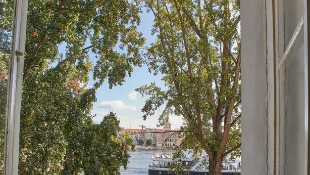 Une vue depuis une fenêtre donnant sur une rivière, avec des bateaux, un arbre et un bâtiment en arrière-plan.