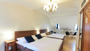 Une chambre d’hôtel avec deux lits, une tête de lit en bois, des tables de chevet, un lustre, un bureau avec une chaise et un grand miroir.