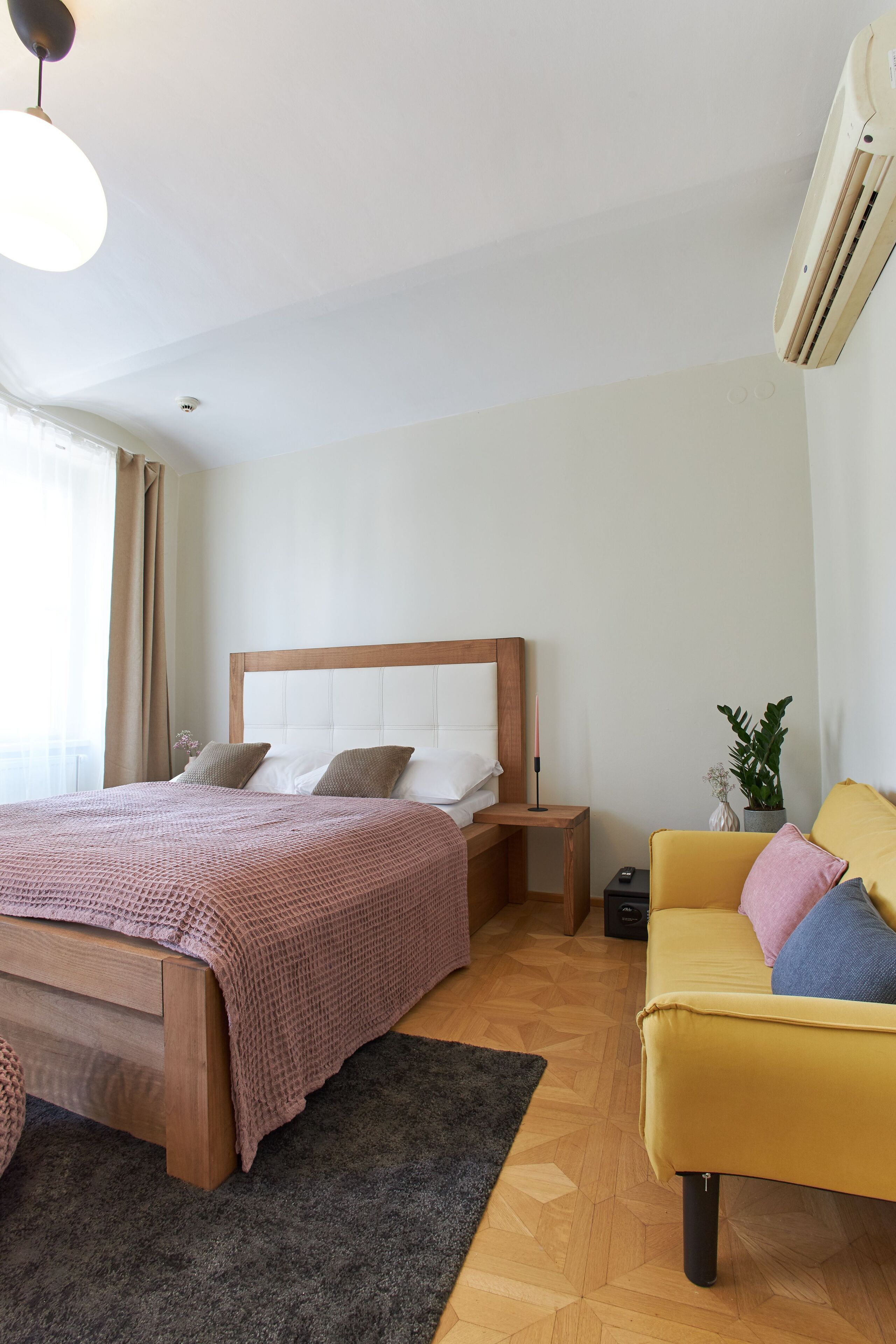A modern bedroom with a wooden bed, a yellow armchair, a small bedside table, and a potted plant.