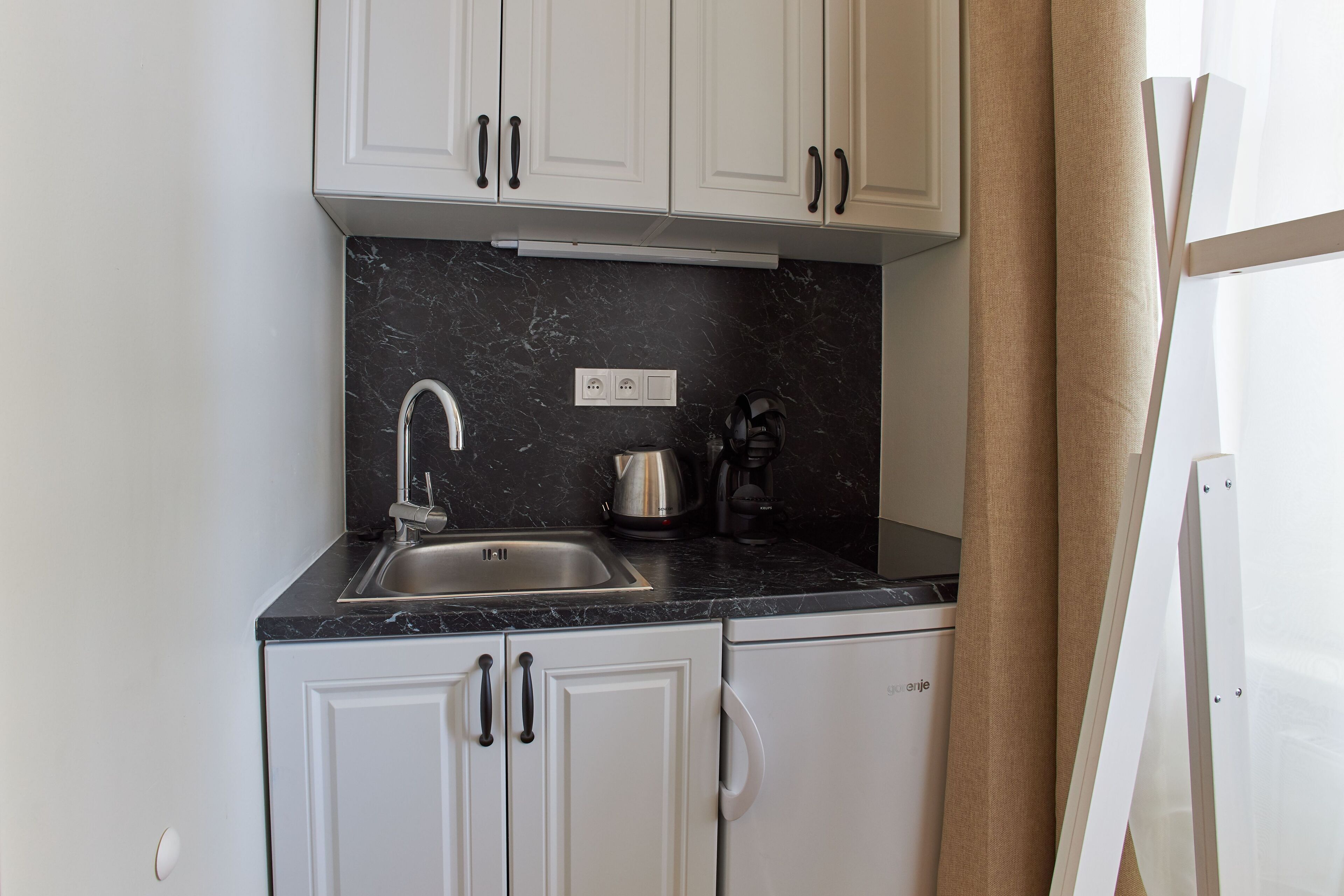 A compact kitchen with white cabinets, a black marble countertop, a stainless steel sink, and a coffee maker.