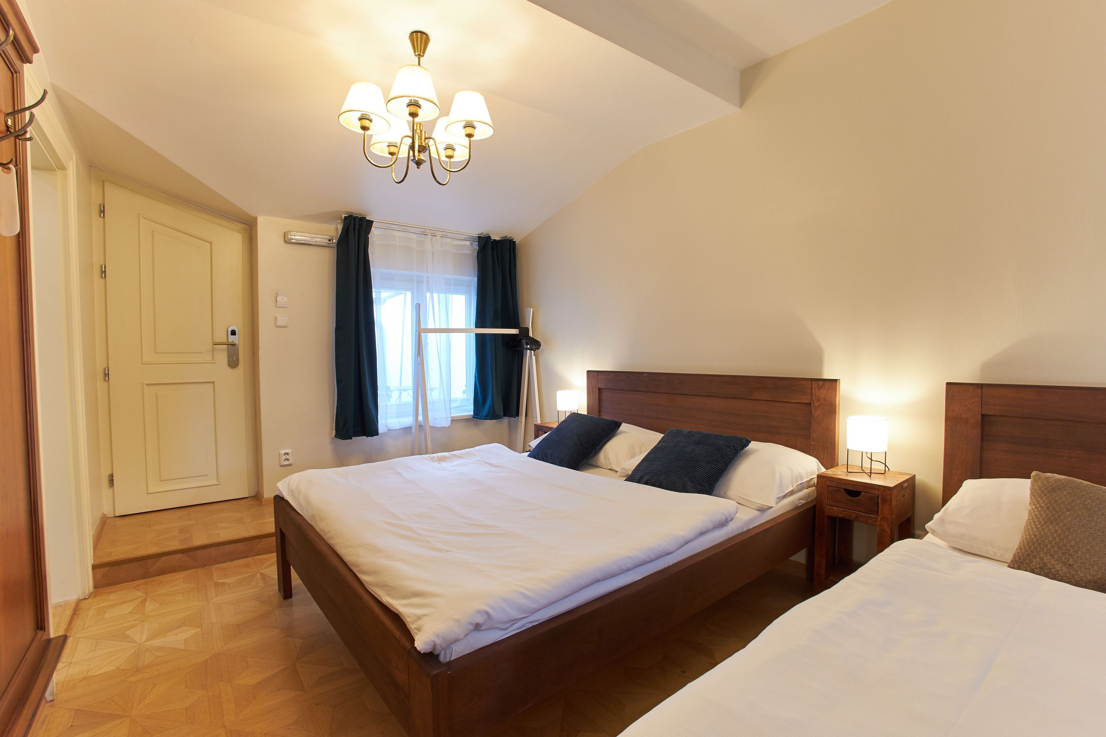 Hotellihuone, jossa on suuri sänky, yöpöytä lampun kanssa, puinen sängynpääty ja kattokruunu.