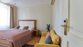 A hotel room with a bed, a sofa, a nightstand, a small table, and a potted plant.