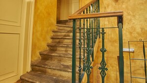 Un escalier avec des marches en pierre et des rampes en métal vert, menant à l’étage supérieur.