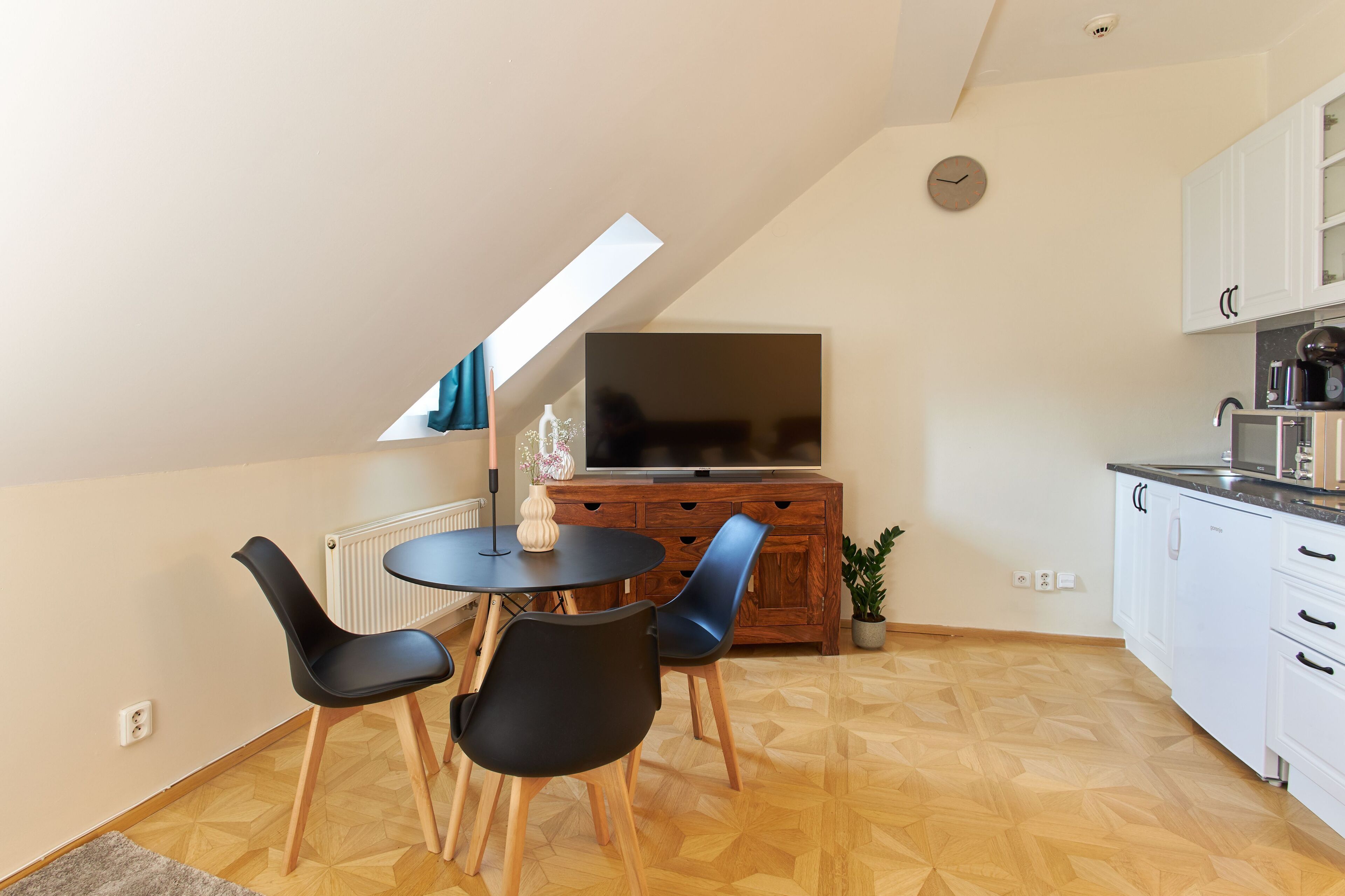 A modern kitchen with a dining area, a large TV, and a skylight.