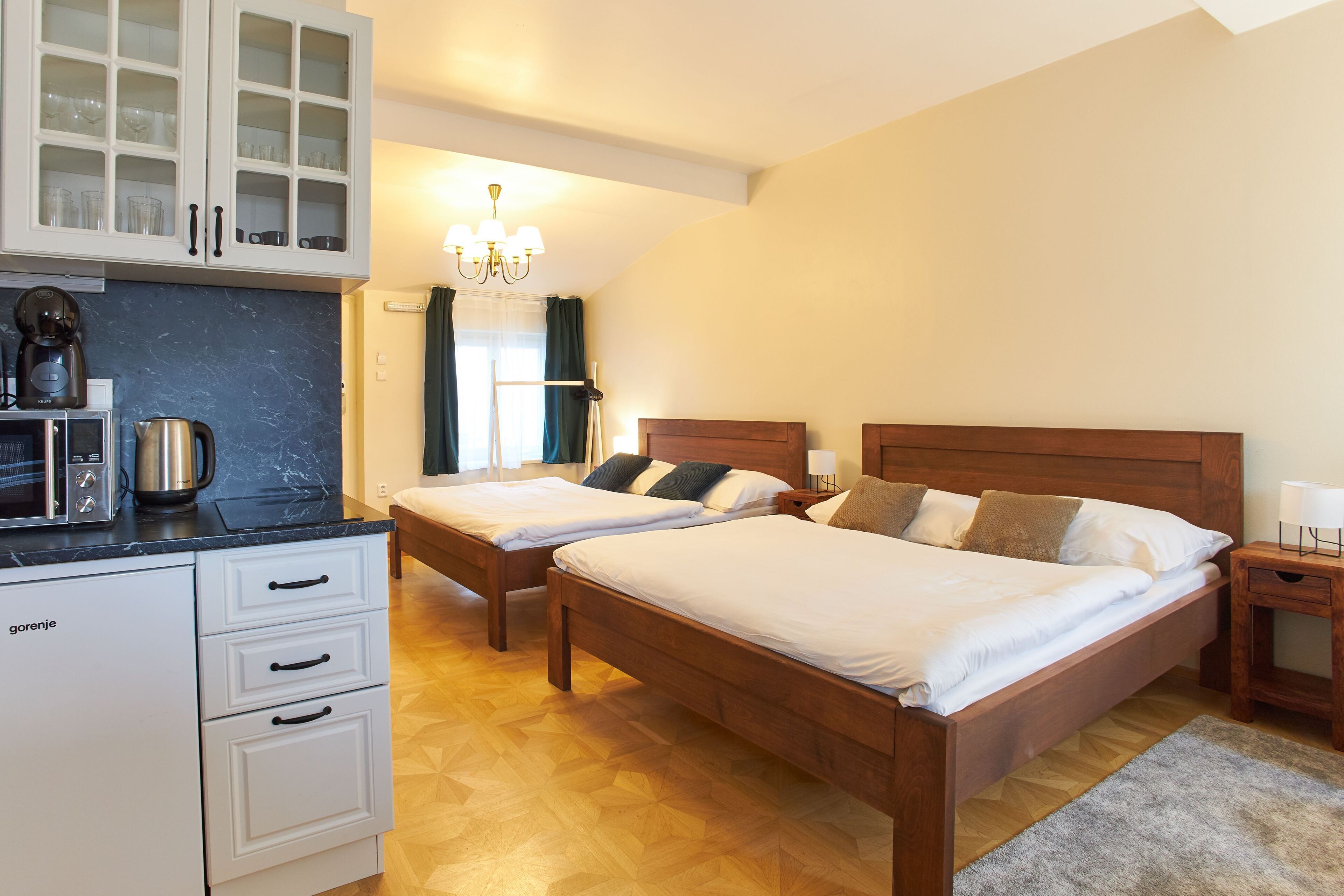 Een slaapkamer met twee bedden, een kitchenette en een kroonluchter.