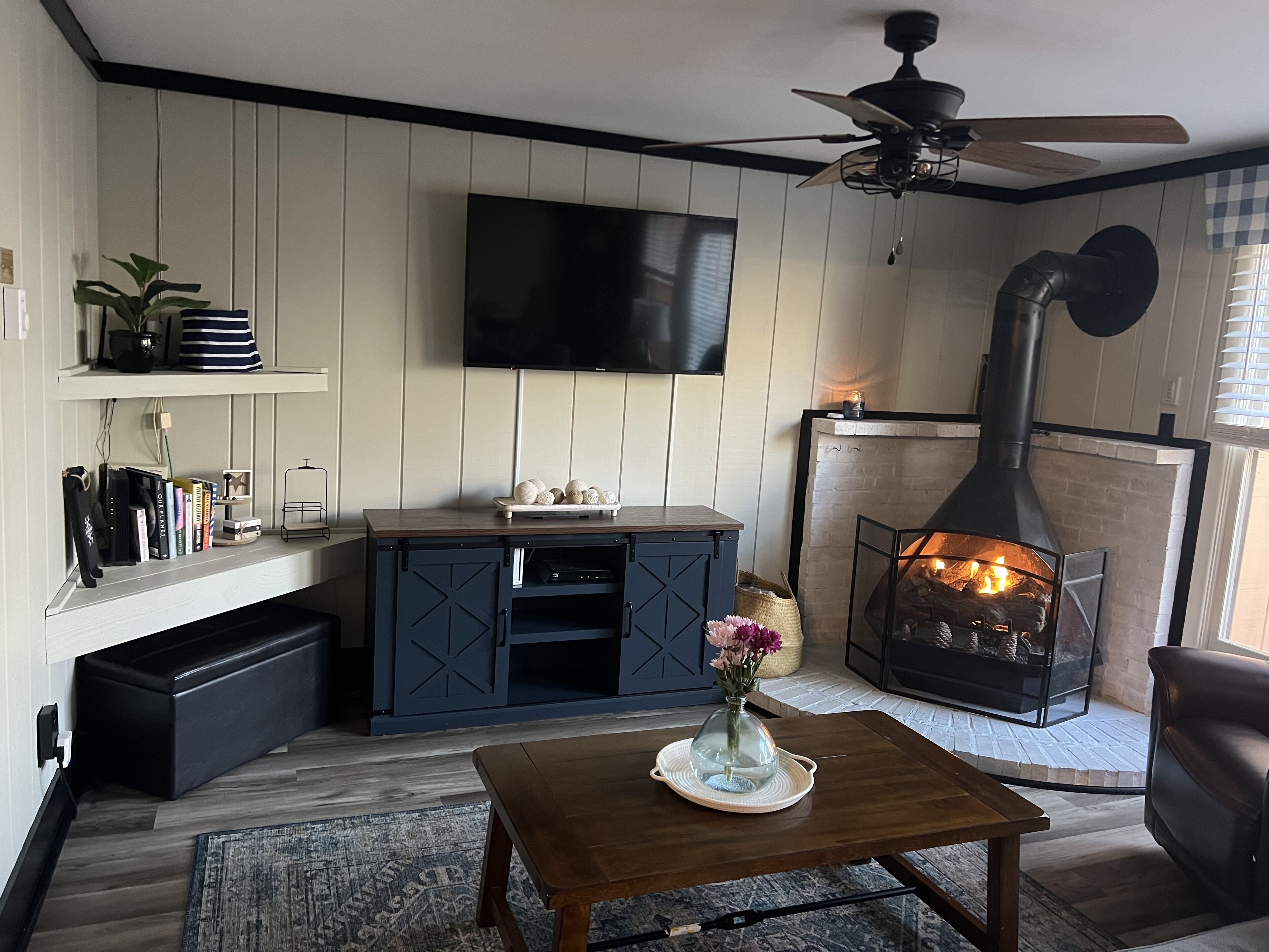 Ein gemütliches Wohnzimmer mit Kamin, Wandfernseher und Deckenventilator.