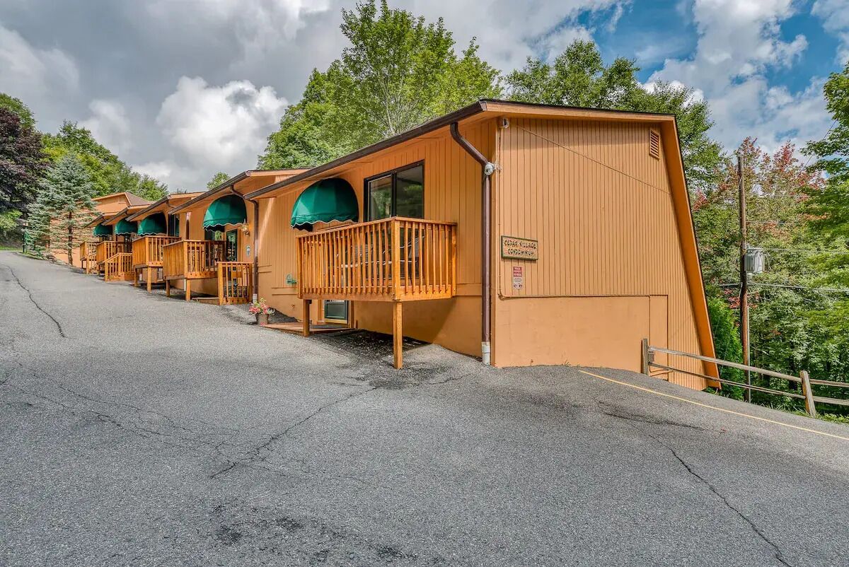 A row of wooden cabins with balconies, a sign indicating a campground, and a paved road leading to them.