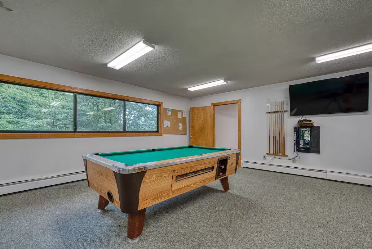 Une table de billard dans une pièce dotée d’une grande fenêtre, d’un téléviseur et d’un radiateur.