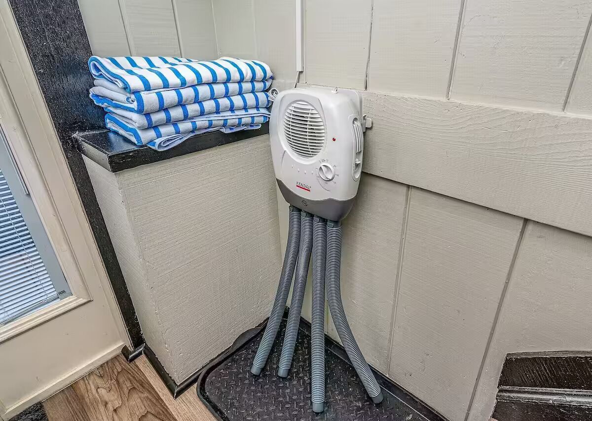 Canto de um quarto com um secador de cabelo fixado na parede e uma pilha de toalhas dobradas em uma prateleira.