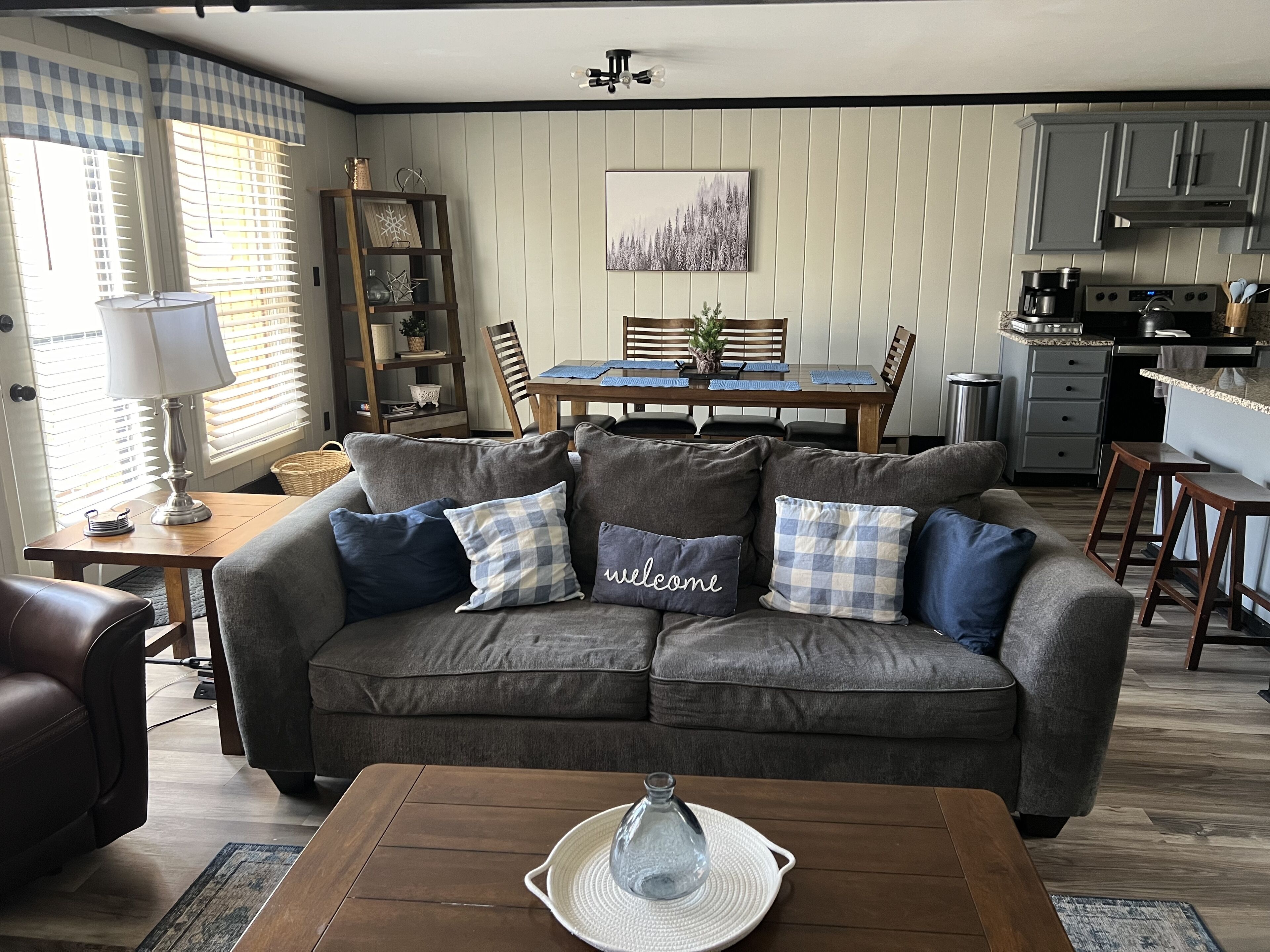 Un salon chaleureux avec un canapé gris, une table basse et un coin repas comprenant une table et des chaises en bois.
