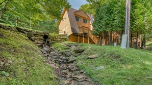 A house with a stone staircase leading to a wooden deck, surrounded by lush greenery and a stone wall.