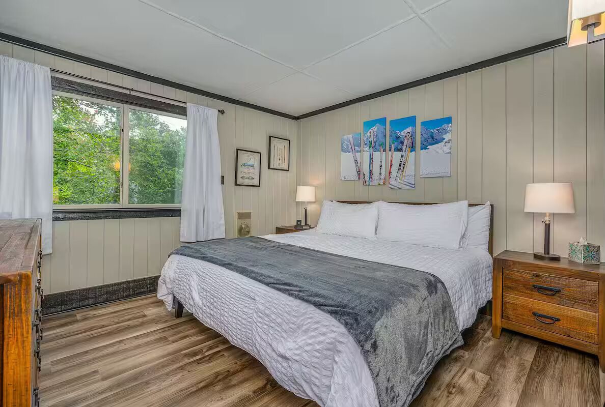 Ein Schlafzimmer mit einem großen Bett, Holzböden, einem Fenster mit Vorhängen und Wandlampen.