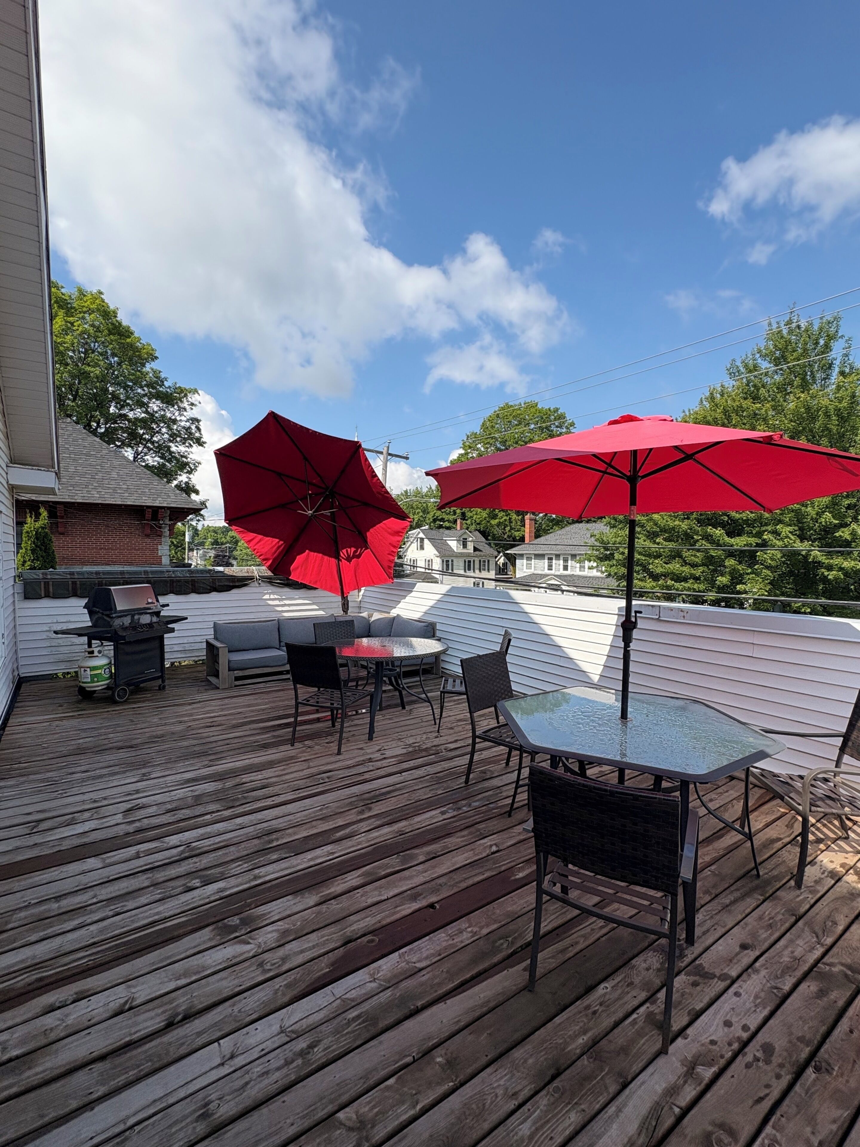 A wooden deck with outdoor furniture, including a table and chairs, and two red umbrellas.