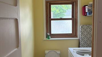 A compact bathroom with a toilet, a window, and a washing machine.