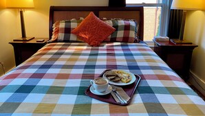 Quarto de hotel com colcha xadrez, bandeja com café da manhã e duas luminárias de cada lado da cama.