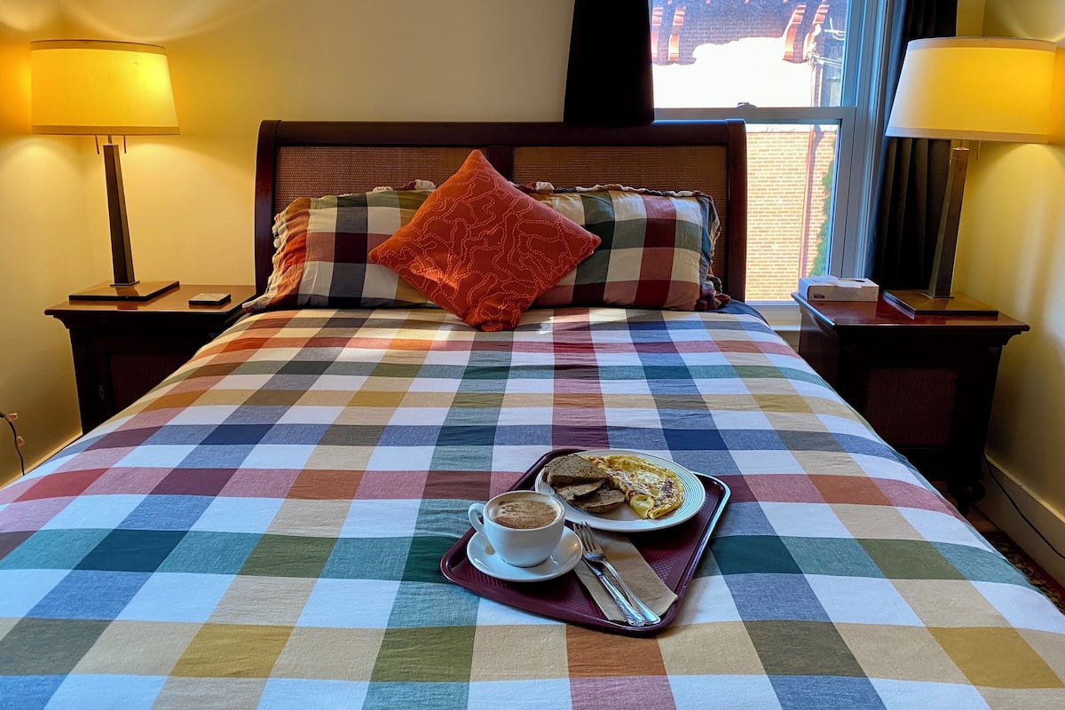 A hotel room with a checkered bedspread, a tray with breakfast, and two lamps on either side of the bed.
