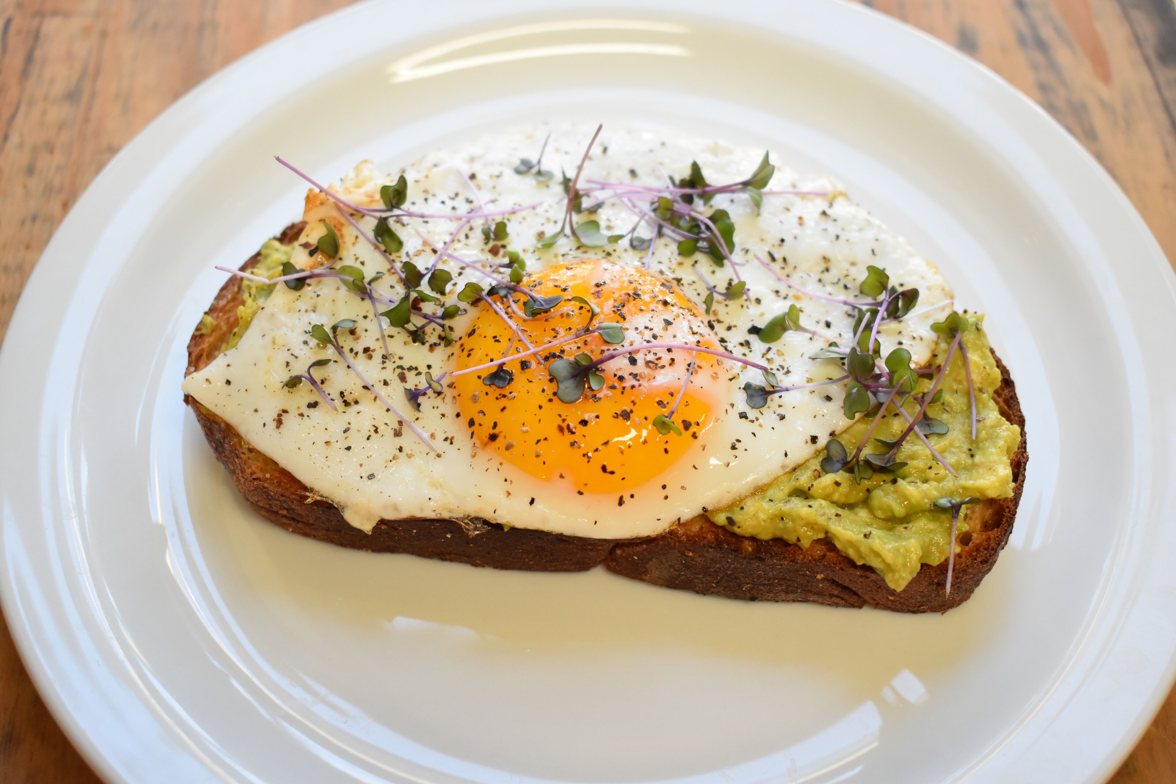 A plate with a fried egg, avocado, and greens on toast.