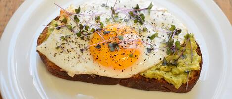 A plate with a fried egg, avocado, and greens on toast.