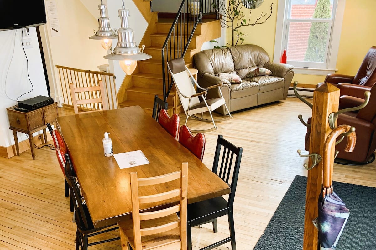 A spacious living area with a wooden dining table, multiple chairs, a sofa, and a staircase leading to another level.