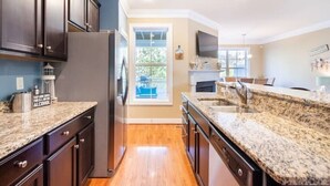 A kitchen with dark wooden cabinets, granite countertops, a stainless steel refrigerator, and a window with a view of greenery. - Rehoboth Beach Home with Pool and Dedicated Workspace! (Rehoboth Beach)
