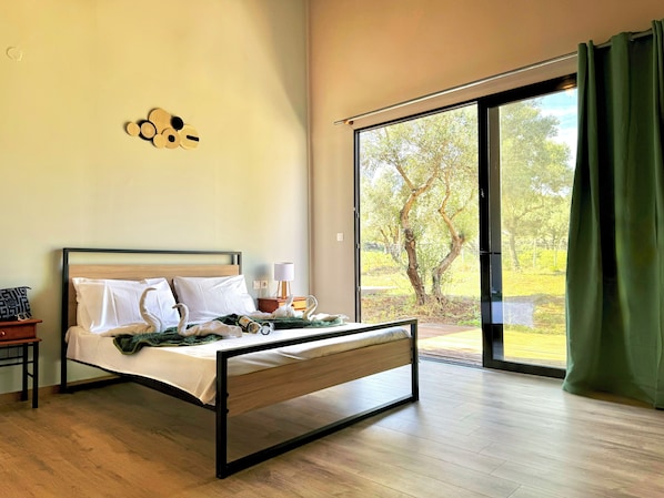 Une chambre moderne avec un lit, une table de chevet, une lampe et une vue sur un jardin, accessible par une porte coulissante.