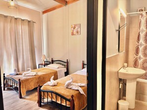 A hotel room with two beds, a bathroom with a sink and mirror, and a shower curtain. - Minimalist  home with common pool (Chania)