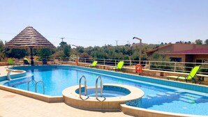 Piscina com hidromassagem, rodeada por espreguiçadeiras e uma cobertura de palha.