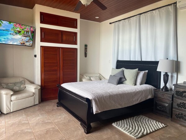 A bedroom with a bed, a chair, a nightstand, and a television mounted on the wall. - Villa Del Mar 1. 180°, SPECTACULAR Ocean View, Gated community (Savegre de Aguirre)