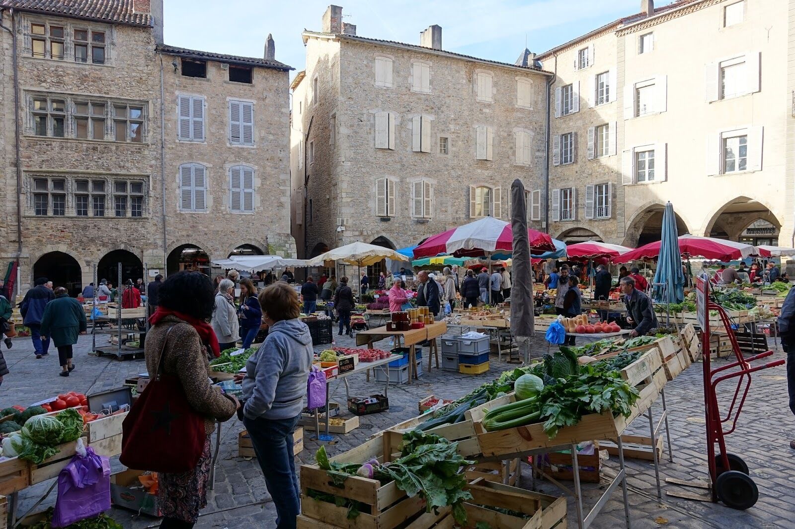 Un marché animé en plein air où des vendeurs proposent des produits frais sous des parasols aux couleurs vives.