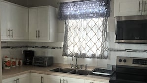 A compact kitchen with white cabinets, a microwave, a stove, and a sink.
