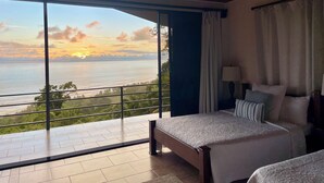 Ein Schlafzimmer mit großem Fenster und Blick auf das Meer und grüne Natur.