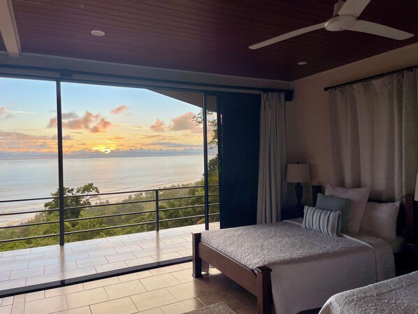 A bedroom with a large window overlooking a scenic view of the sea and greenery.