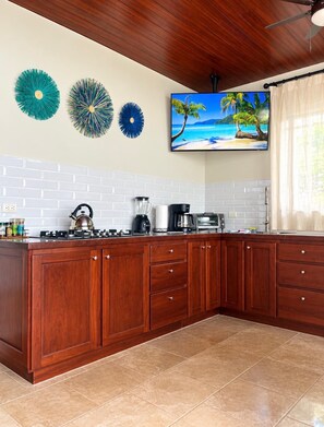 A kitchen with a wooden countertop, white tiled backsplash, and a television displaying a beach scene. - Villa Del Mar 2. 180°, SPECTACULAR Ocean View, Gated community (Savegre de Aguirre)