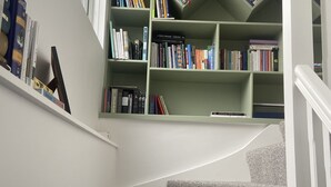 Een trap met een gestreept tapijt, een boekenplank vol boeken en een raam op de achtergrond.