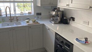 Een moderne keuken met een ingebouwde wasmachine, een koffiezetapparaat en een raam met jaloezieën.