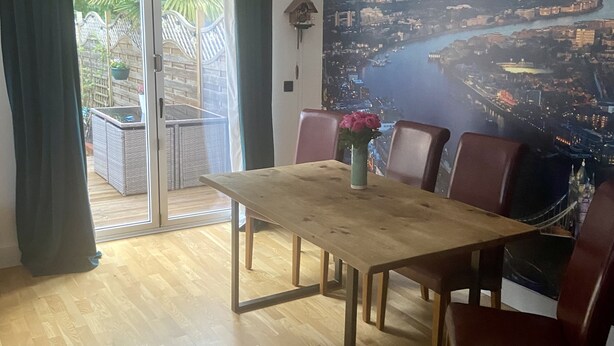 Een eethoek met een houten tafel en stoelen, een uitzicht op een stadsbeeld door een groot raam en een schuifpui naar een balkon.