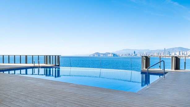 Una piscina con terraza de madera y vista a un paisaje urbano.